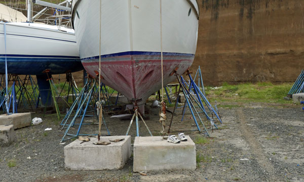 Sailboat in storage cradle secured by tensioned webbing tie-downs to concrete blocks