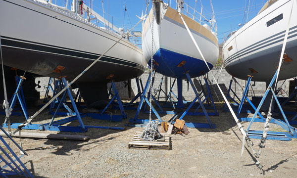 Sailboat in storage cradle secured by tensioned webbing tie-downs to ground anchors