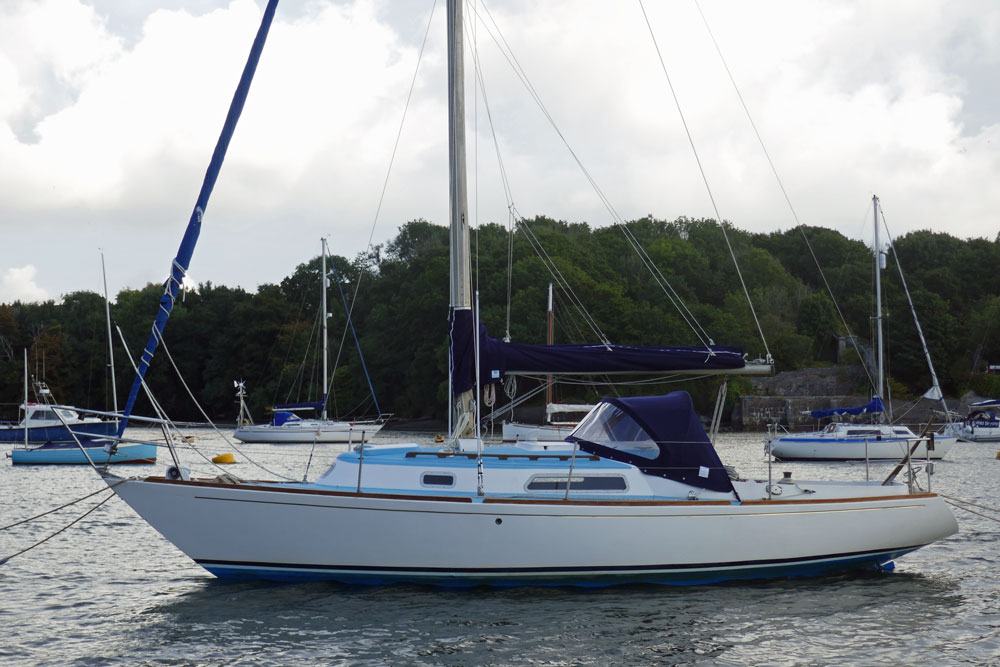 A Hustler 30 sailboat moored on the UK's River Tamar with the Cornish shore in the background.