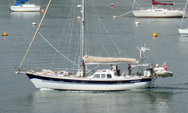 A cutter-rigged sailboat motors down the River Tamar towards Plymouth Sound and the open sea.